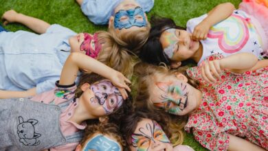 Group of children enjoying an outdoor party with colorful face paint, lying on grass.