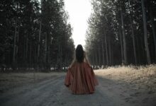 woman holding her brown dress in the middle of forest