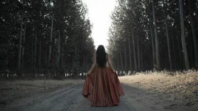 woman holding her brown dress in the middle of forest