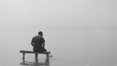 grayscale photo of man sitting on dock