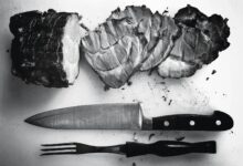 grayscale photo of grilled meat beside knife and fork