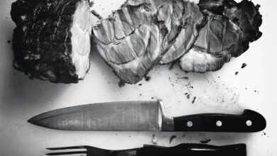 grayscale photo of grilled meat beside knife and fork