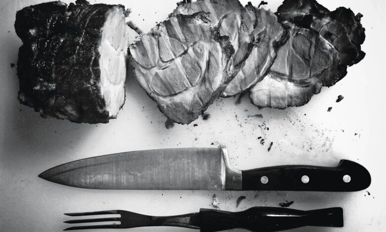 grayscale photo of grilled meat beside knife and fork