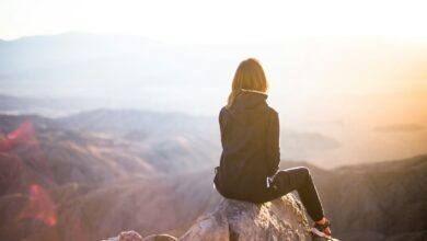 person sitting on top of gray rock overlooking mountain during daytime